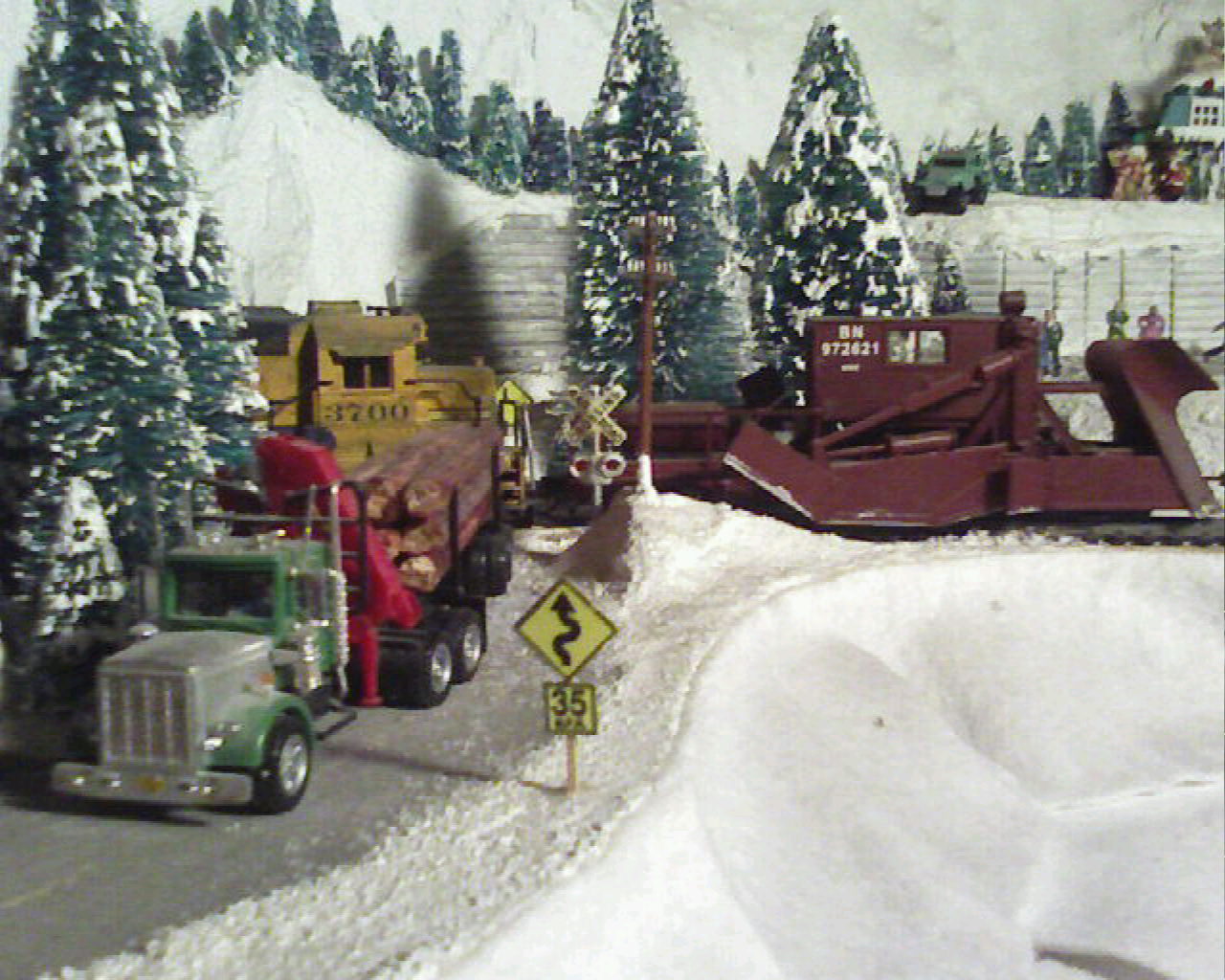 A log truck crosses the tracks just in frount of a Jordan Spreader on Wolf 