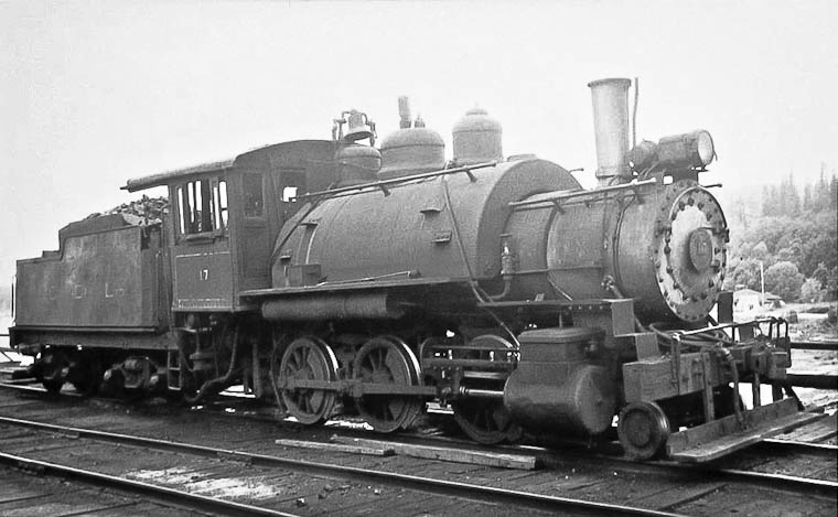 A logging locomotive and tender round the bend past an old water