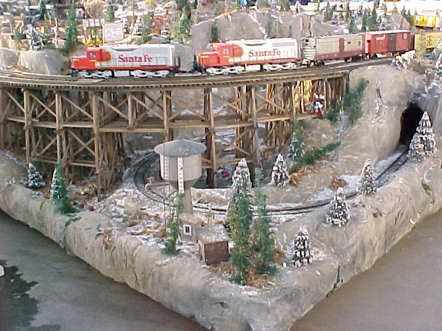 Santa Fe locomotives cross a trestle at a corner of the display.